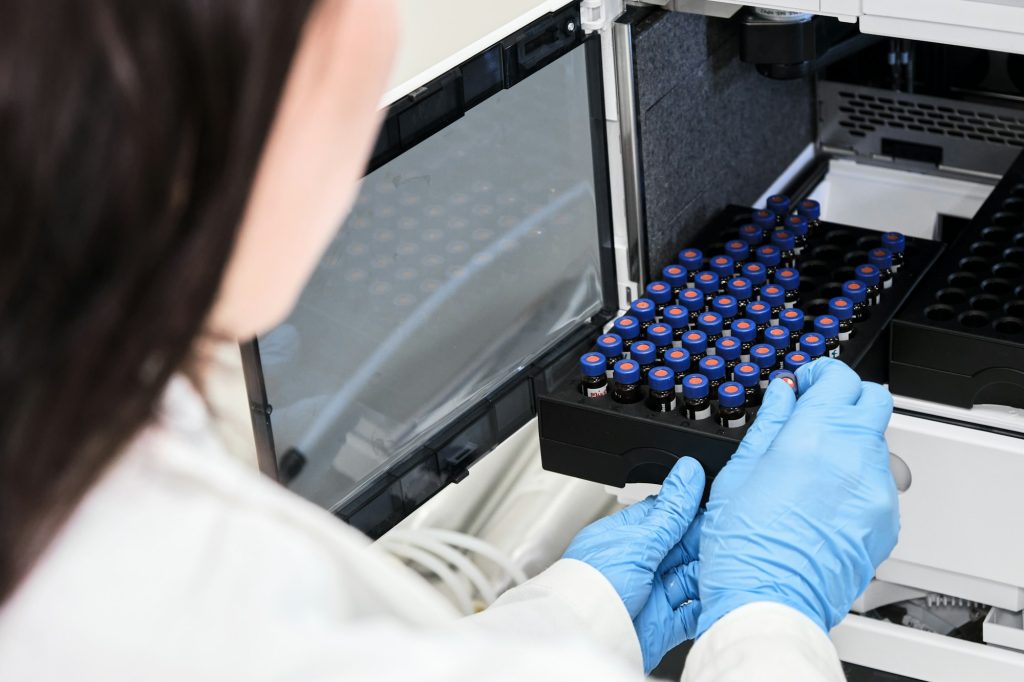 Scientist in a white lab coat putting vial with a sample into autosampler of HPLC system. High